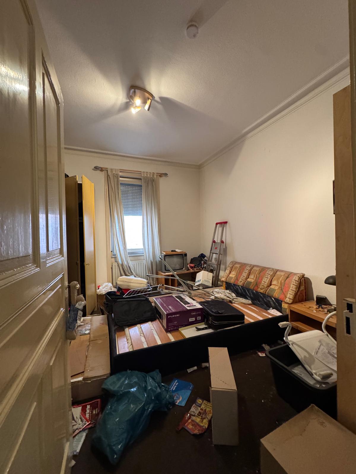 Vorher: vollgestelltes Zimmer mit Bett, Sofa, Kartons und Müll vor der Wohnungsauflösung