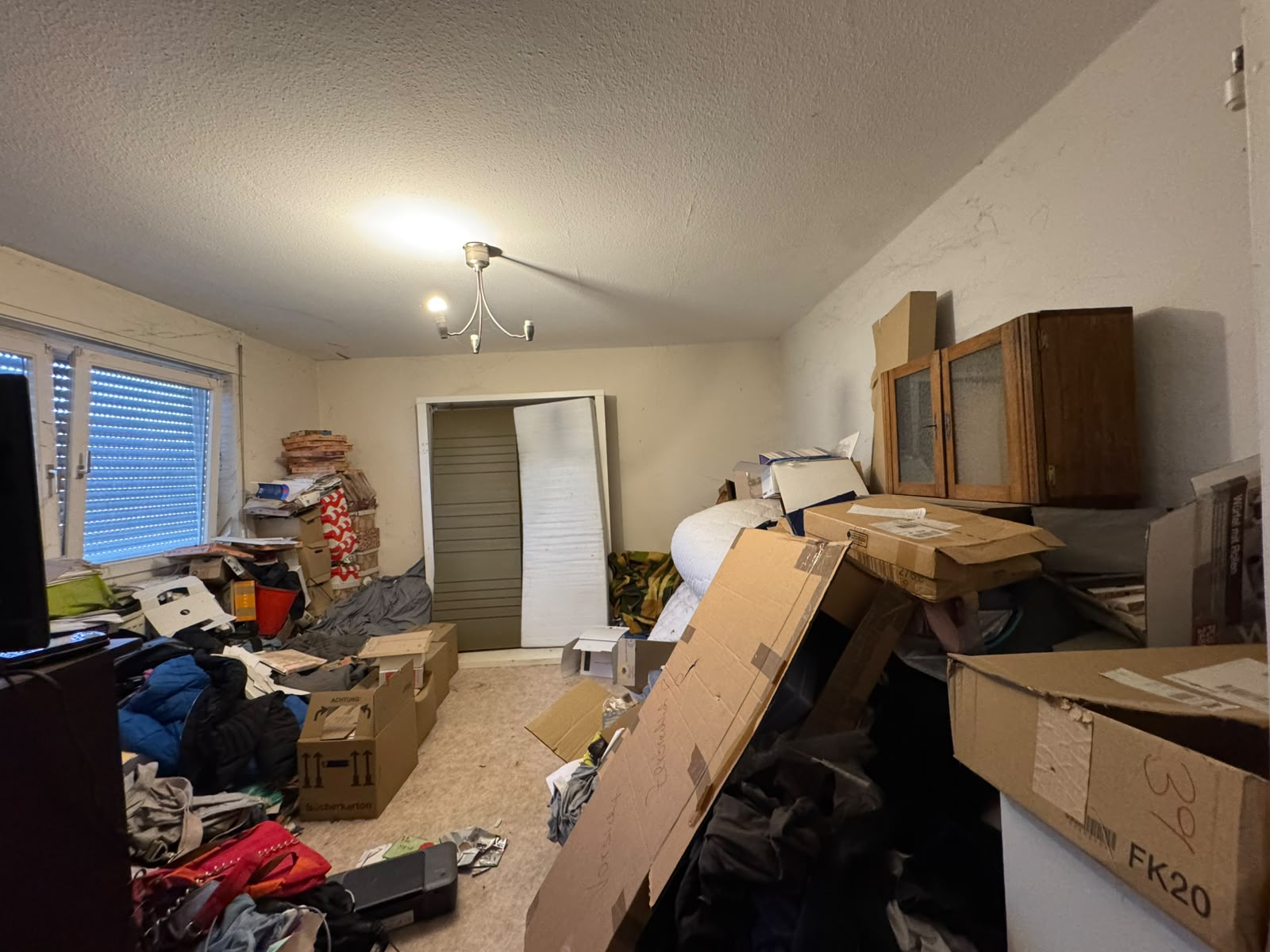Vollgestelltes Zimmer mit Kartons, Kleidung und Möbeln vor der Haushaltsauflösung